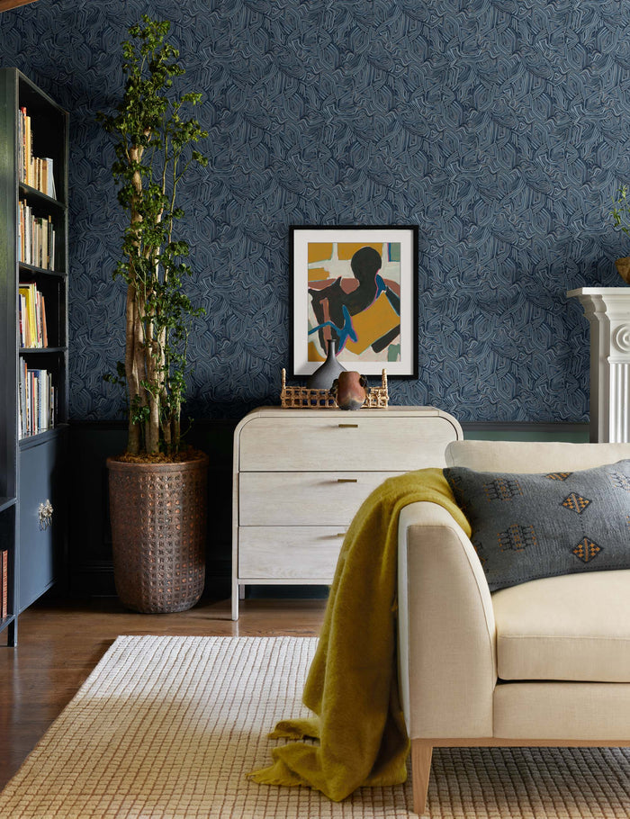 #color::blue #color::indigo #insert::down #insert::polyester | The Indigo woven cotton boho and folk-inspired lumbar pillow with a wool front sits on a beige linen sofa in a living room with indigo patterned walls and colorful decor accents