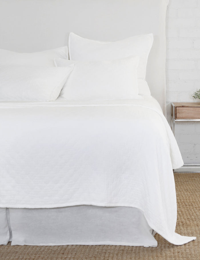 #color::white #size::euro-sham #size::king #size::standard | The Ojai white Cotton Matelassé Sham with a diamond woven pattern by Pom Pom at Home lays on a white linen framed bed in a bedroom with a white brick wall, a jute rug, and a wooden nightstand