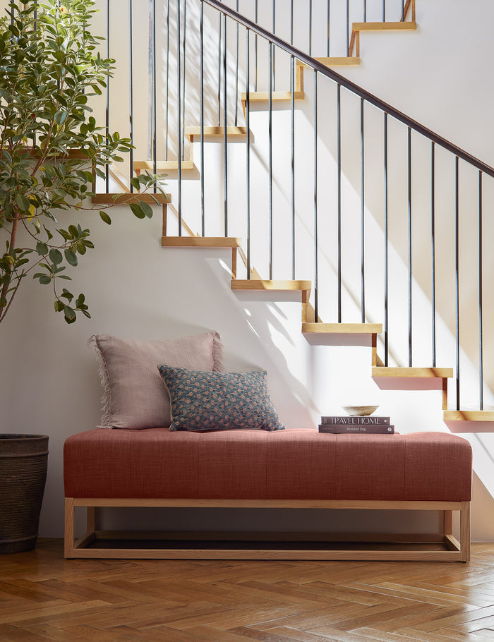 #size::13--x-20- | Tamra blue and pink lumbar pillow with floral patterns sits on a red linen bench in a room with a staircase in the background