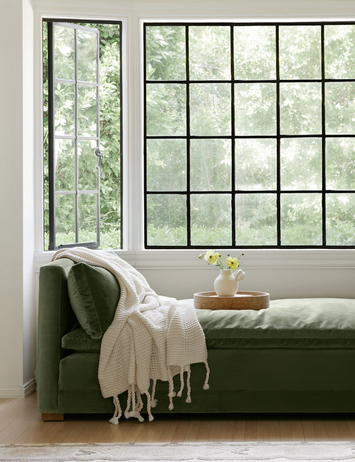 #color::white | The Trestles white chunky knit throw by pom pom at home lays atop sage velvet bench in a nook with a cork tray and white vase