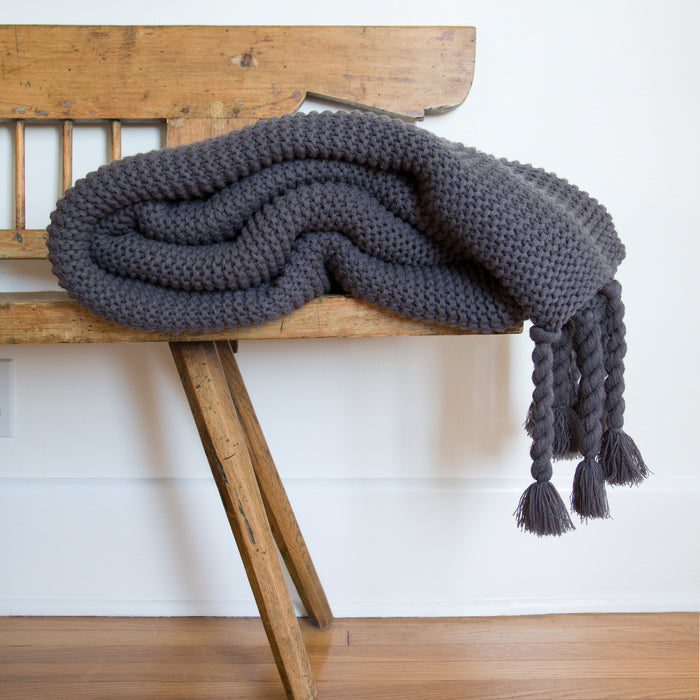 #color::midnight | The Trestles midnight gray chunky knit throw by pom pom at home lays atop a wooden bench